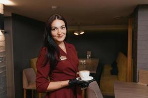 Eine Restaurantmanagerin trägt eine schwarze Gesichtsmaske und Einweghandschuhe mit einer Tasse Kaffee in einem Restaurant foto