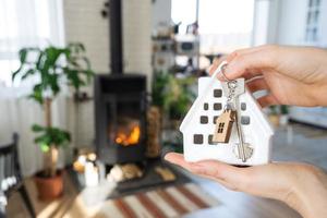 Schlüssel zum Haus mit Schlüsselanhänger vor dem Hintergrund des Kaminofens mit Feuer und Brennholz. gemütlicher Herd zu Hause. Bau, Design, Projekt, Umzug in ein neues Haus, Hypothek, Miete und Kauf von Immobilien foto