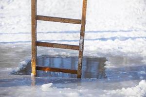 ein Eisloch im ein Winter See mit ein hölzern Leiter. Fest von das Taufe von Jesus. foto