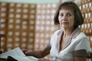 Alten Frau Bibliothekar mit ein Buch auf das Hintergrund von Bibliothek Schränke mit Zellen. foto