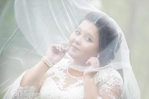das Fett Braut versteckte im ein Hochzeit Schleier gegen das Hintergrund von Natur. foto