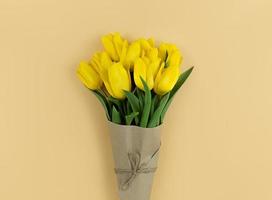 Strauß gelber Tulpen, eingewickelt in Bastelpapier auf beigem Hintergrund foto