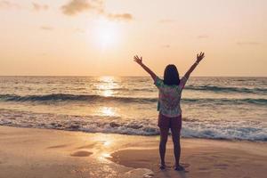 eine Frau, die ihre Hände während der Sommerferien an einem Strand zum Himmel erhebt foto