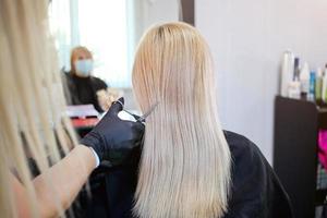 Friseur mit Sicherheit Maße zum COVID-19, ein Frau im ein medizinisch Maske, Sozial Distanz, Schneiden Haar mit ein medizinisch Maske und Gummi Handschuhe im ein Schönheit Salon. foto