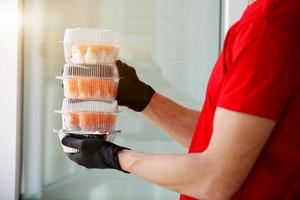 ein Mann Hände Gummi Handschuhe mit ein Plastik Behälter mit Sushi und Rollen. foto