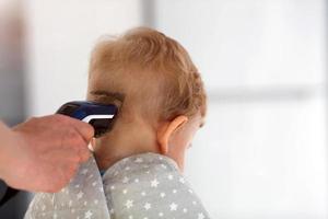 weiblich Hände Schnitt ein Kind mit ein Haar Clipper im ein Friseur. das zuerst Haarschnitt. foto