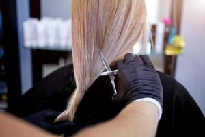 Hände von ein Friseur im Gummi Handschuhe Schnitt blond ist Schwanz. Frau bekommen ein Neu Haarschnitt. foto