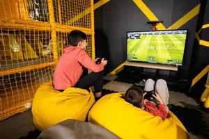 zwei Brüder spielen Fußball Video Spiel Konsole, Sitzung auf Gelb Puff im Kinder abspielen Center. foto