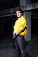 ein asiatisch Mann mit glatt schwarz Haar tragen ein Gelb Jacke und Jeans während posieren foto