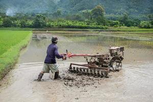 thailändisch Bauern Arbeiten mit ein Handheld Motor- Pflug im ein Reis Feld foto