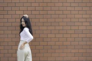 Porträt von Hipster Mädchen auf Backstein Mauer Hintergrund, schön asiatisch Frau Pose zum nehmen ein Foto, kawaii Stil foto