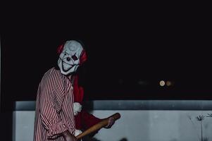 asiatisch gut aussehend Mann tragen Clown Maske mit Waffe beim das Nacht Szene, Halloween Festival Konzept, Schrecken unheimlich Foto von ein Mörder im Orange Tuch, böse Clown Charakter