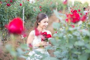 jung asiatisch Frau tragen ein Weiß Kleid posiert mit ein Rose im Rose Garten foto