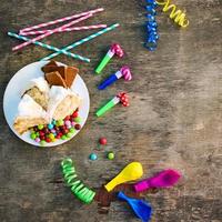 Kuchen, Süssigkeit, Schokolade, Pfeifen, Streamer, Luftballons auf Urlaub Tisch. Konzept von Kinder- Geburtstag Party. Aussicht oben. foto