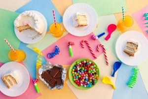 Kuchen, Süssigkeit, Schokolade, Pfeifen, Streamer, Luftballons auf Urlaub Tisch. Konzept von Kinder- Geburtstag Party. Aussicht oben. foto