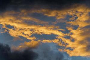 golden flauschige Wolken beleuchtet verschwinden Strahlen beim Sonnenuntergang und Gewitterwolken über sonnig Blau Himmel foto