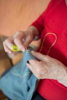 unkenntlich Senior Frau tun Stickerei mit ein Gelb Fingerhut foto