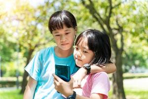 zwei Schwestern umarmen während mit Handy, Mobiltelefon Telefon im das Park. glücklich Familie Konzept. foto