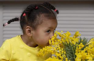 wenig afrikanisch amerikanisch Mädchen schnüffeln Gelb Blumen. foto