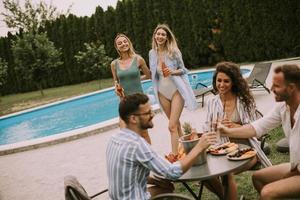 Gruppe junger Leute, die mit Apfelwein am Pool im Garten jubeln foto