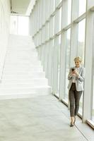 Geschäftsfrau mit Handy auf modernen Büroflur foto