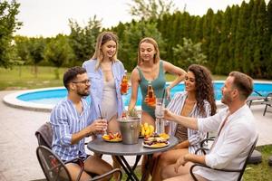 Gruppe junger Leute, die mit Apfelwein am Pool im Garten jubeln foto