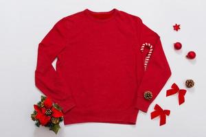 Schließen Sie herauf rotes leeres Schablonensweatshirt mit Kopienraum und Weihnachtsfeiertagskonzept. draufsicht-modell-hoodie und rote feiertagsdekorationen auf weißem hintergrund. frohes neues jahr zubehör. Weihnachts-Outfit foto