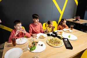 vier Kinder Essen Italienisch Pizza im Pizzeria. Kinder Essen beim Cafe. foto