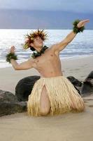 jung männlich Hula Tänzer kniend zurück auf das Sand im ein traditionell hawaiisch Hula Pose. foto