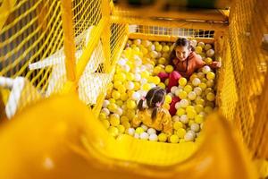 Geschwister abspielen mit farbig Bälle beim Gelb Spielplatz Park. Schwestern im aktiv Unterhaltungen. foto