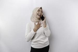 ein glücklich asiatisch Muslim Frau tragen ein Kopftuch, halten ihr Telefon, isoliert durch Weiß Hintergrund foto