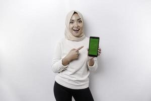ein glücklich asiatisch Muslim Frau tragen ein Kopftuch, zeigen ihr Telefon Bildschirm, isoliert durch Weiß Hintergrund foto