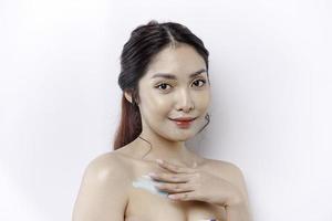 Haut Pflege Produkte Konzept. asiatisch Frau bewirbt sich feuchtigkeitsspendend Lotion auf Körper nach Dusche, Stehen eingewickelt im Handtuch, abgeschnitten Bild foto