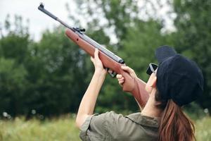 Frau auf Natur Ziel oben Gewehr Jagd zurück Aussicht schwarz Deckel frisch Luft Grün foto