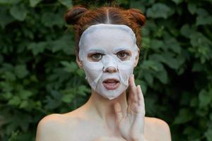 nett Mädchen Antialterung Maske berühren Ihre Gesicht mit Ihre Hand Haut Pflege Blätter im das Hintergrund foto