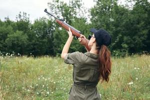 Frau auf draussen halten ein Gewehr oben Grün Overall Jagd Lebensstil schwarz Deckel foto