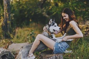 Frau und ihr heiser Hund glücklich spielen draußen im das Park unter das Bäume Lächeln mit Zähne im das Herbst gehen mit ihr Haustier foto