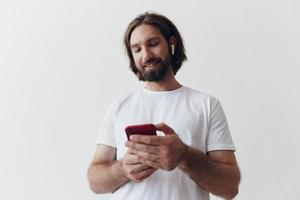 Mann Blogger hält ein Telefon im seine Hände und kommuniziert mit Menschen online im Sozial Netzwerke mit ein Lächeln und ein Weiß T-Shirt auf ein Weiß Hintergrund foto