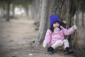 Porträt von süß asiatisch wenig Mädchen tragen Winter Kleider beim das Wald von das parken, thailand Menschen Pose zum nehmen ein Bild, glücklich Zeit foto