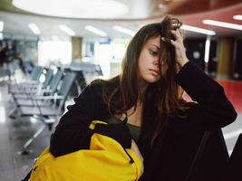 Frau mit Gelb Rucksack sitzt beim das Flughafen während warten zum ein Flug foto