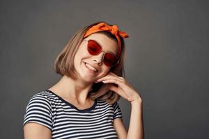 Frau im Sonnenbrille mit ein Orange Binde auf ihr Kopf im ein gestreift T-Shirt Mode foto