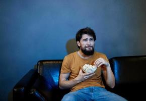 einsam Mann im das Abend auf das Couch im Vorderseite von das Fernseher und Popcorn im ein Teller foto