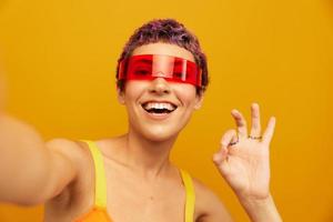 Frau lächelnd im ungewöhnlich Brille tausendjährig nehmen Selfies im Sportbekleidung gegen ein Orange Studio Hintergrund, kostenlos Raum foto