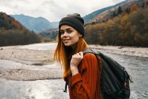 Frau im ein Sweatshirt Deckel mit ein Rucksack auf ihr zurück Berg Fluss im Natur foto