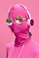 ein verrückt konzeptionelle Porträt von ein jung Frau ohne ein Gesicht Maske auf ein Rosa Hintergrund und tragen glänzend Sonnenbrille Hören zu Musik- auf ihr Kopfhörer. das Konzept von ein Neu Welt und Cyberspace foto