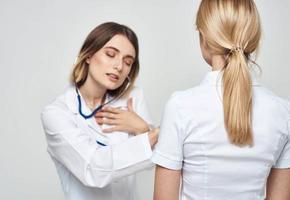 Arzt Frau im ein medizinisch Kleid mit ein Stethoskop kommuniziert mit ein geduldig zurück Aussicht foto