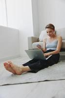 freiberuflich Frau mit Laptop und Telefon funktioniert von Zuhause Sitzung auf das Fußboden im ihr Zuhause Kleider mit ein kurz Haarschnitt, kostenlos Kopieren Raum foto
