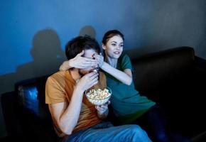 energisch Frau Modell- auf ein Leder Sofa und ein Mann Popcorn im ein Abend Teller foto