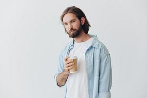 freiberuflich tausendjährig Mann mit Bart Trinken Kaffee von ein Krabbe Tasse im stilvoll Hipster Kleider auf ein Weiß Hintergrund foto