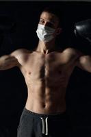 Athlet im ein medizinisch Maske und Boxen Handschuhe auf ein schwarz Hintergrund gepumpt oben Torso foto